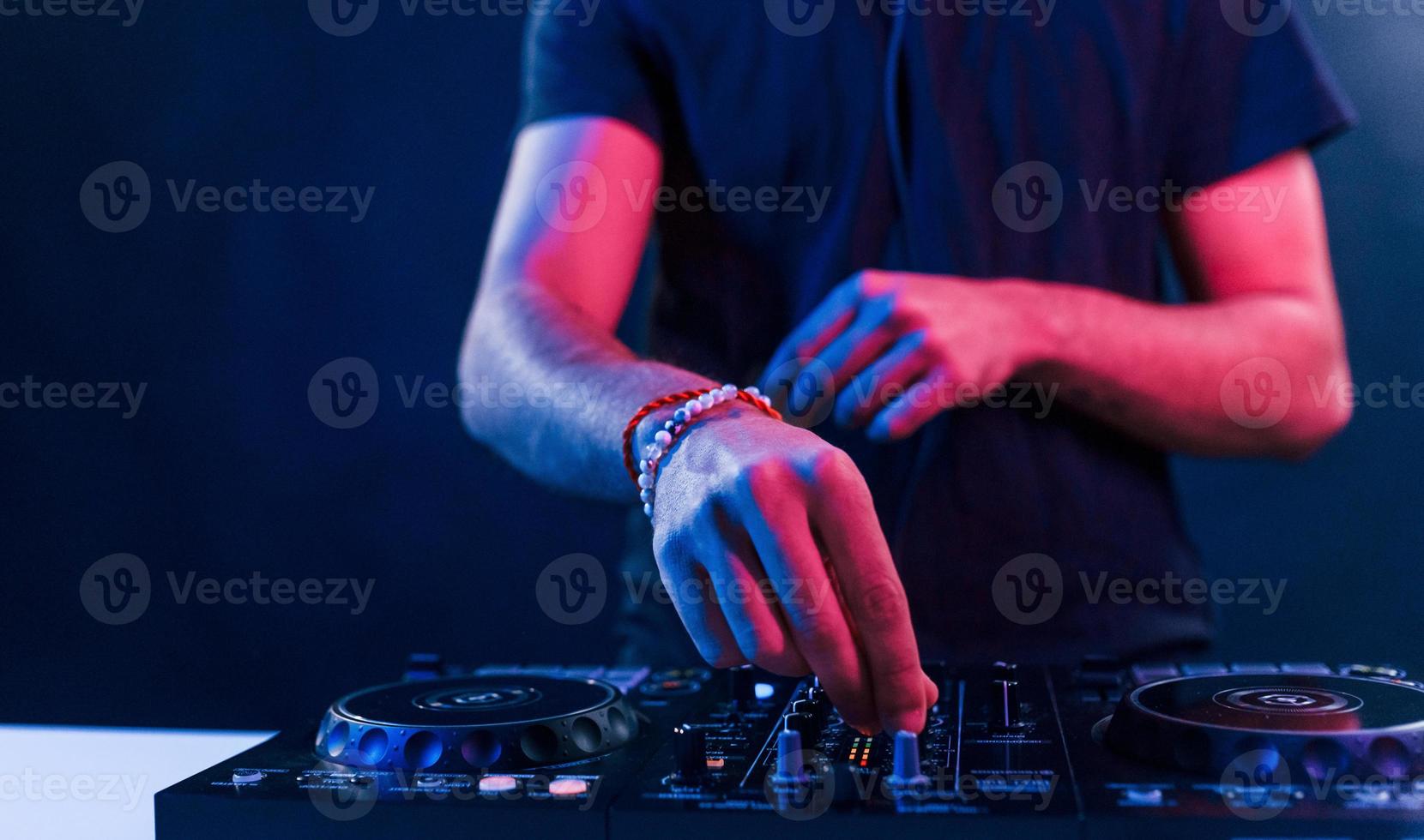 Close up view of DJ's hands that working with music equipment in the club with neon lighting photo