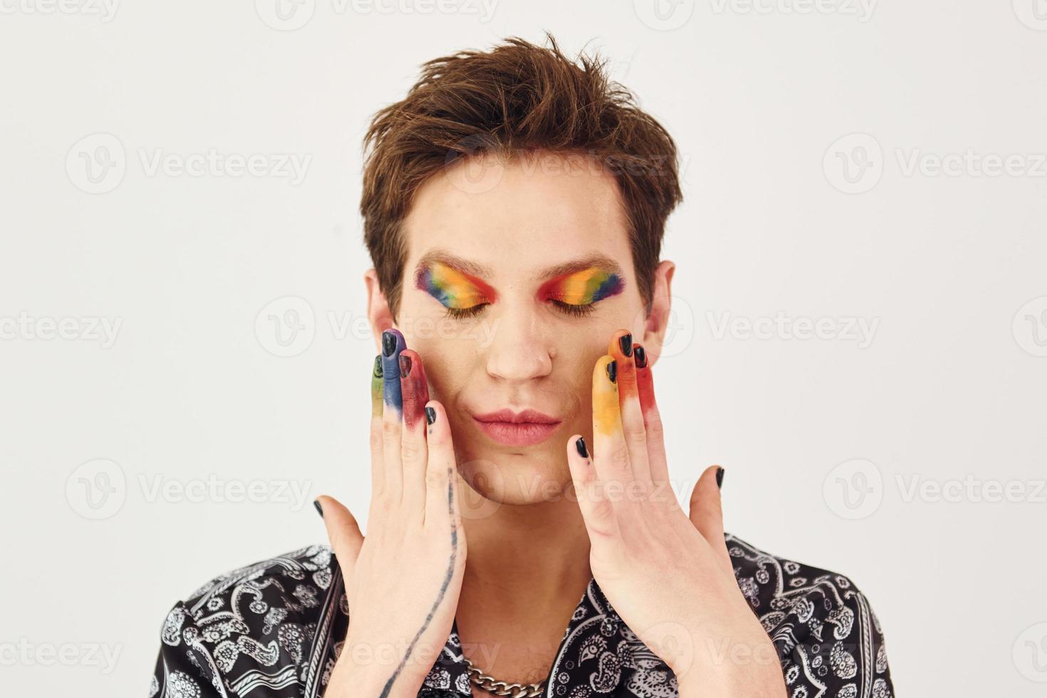 Young gay man is standing in the studio and posing for a camera. Gesturing and doing facial expressions photo