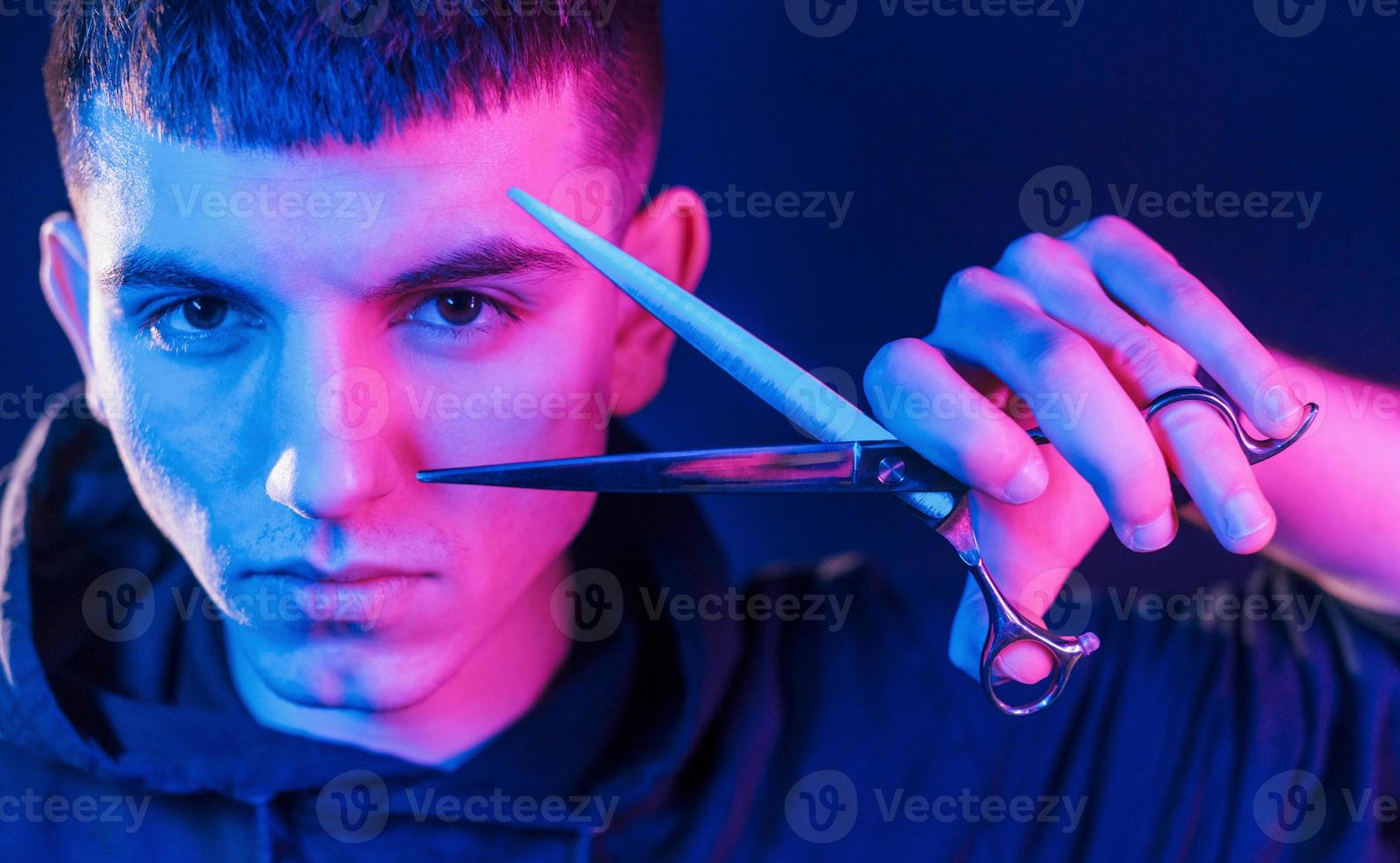 Holds scissors. Young barber with work equipment standing in the studio with neon lighting photo