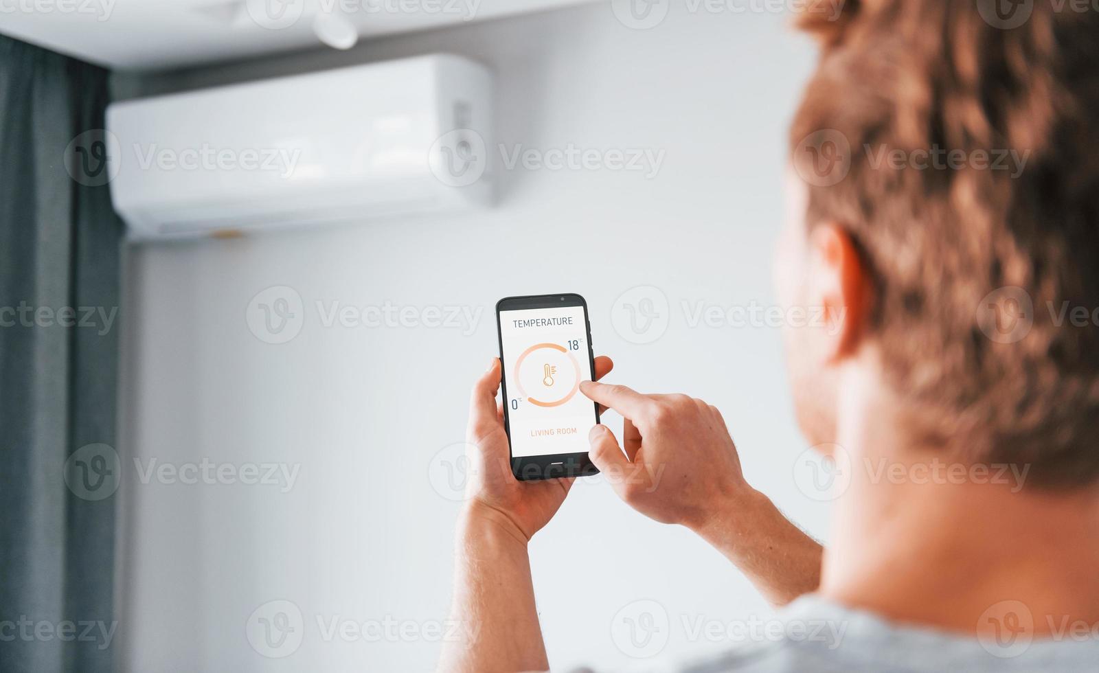 Rear view of adult man that is indoors controlling smart home technology photo