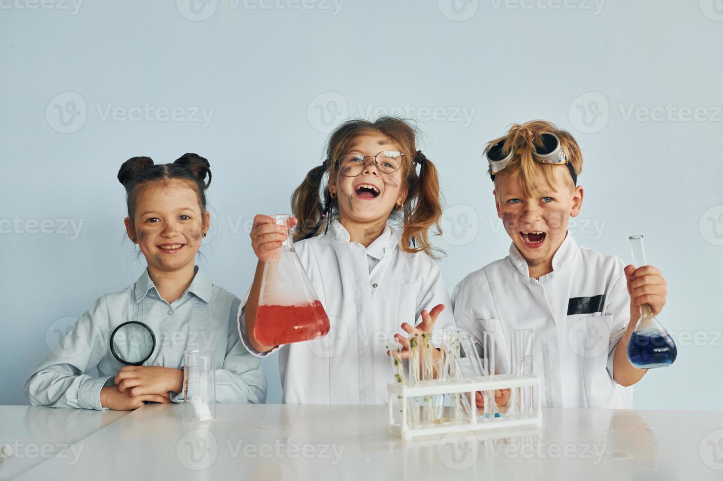 Happy friends smiling. Children in white coats plays a scientists in lab by using equipment photo