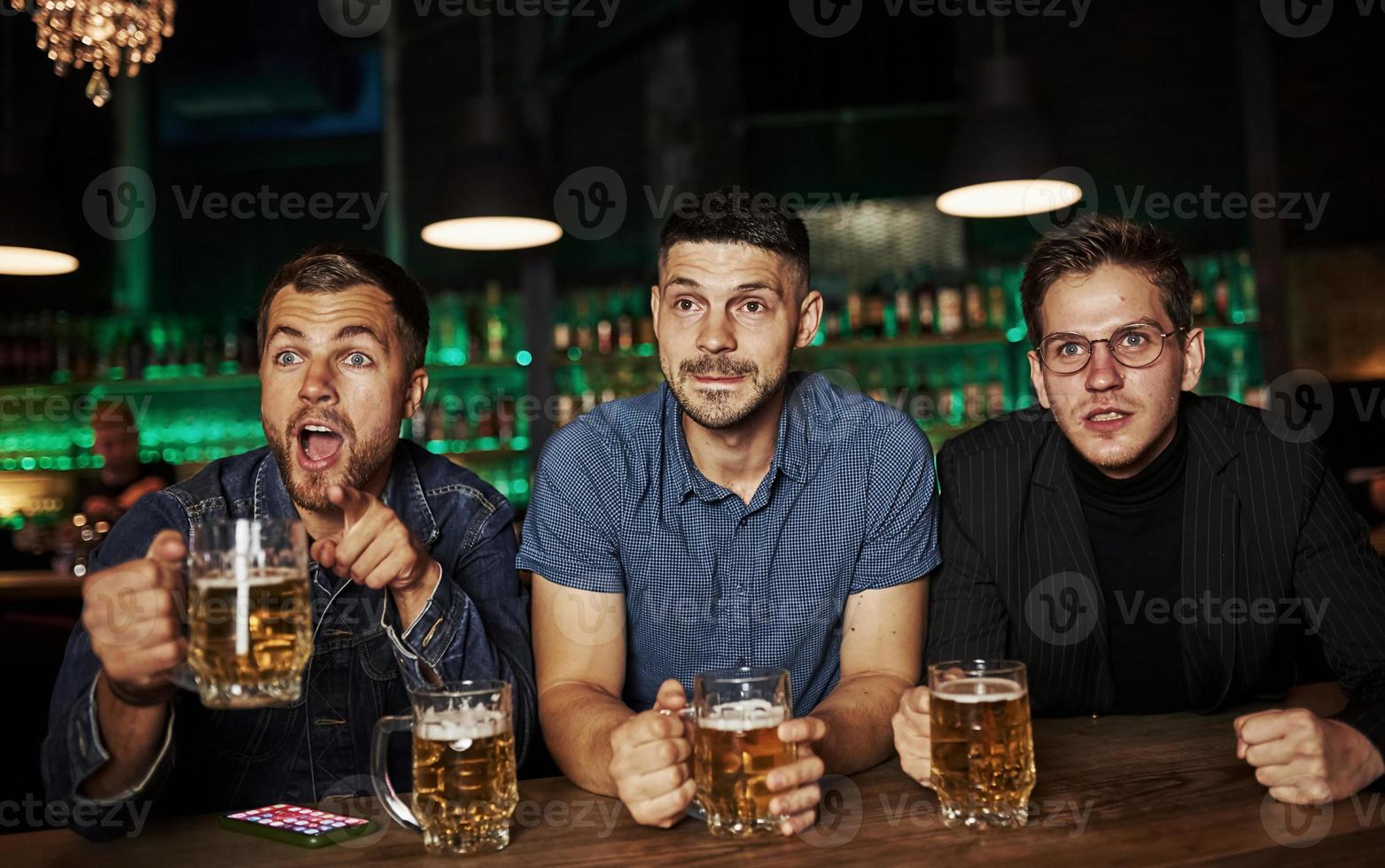 Three sports fans in a bar watching soccer. With beer in hands photo