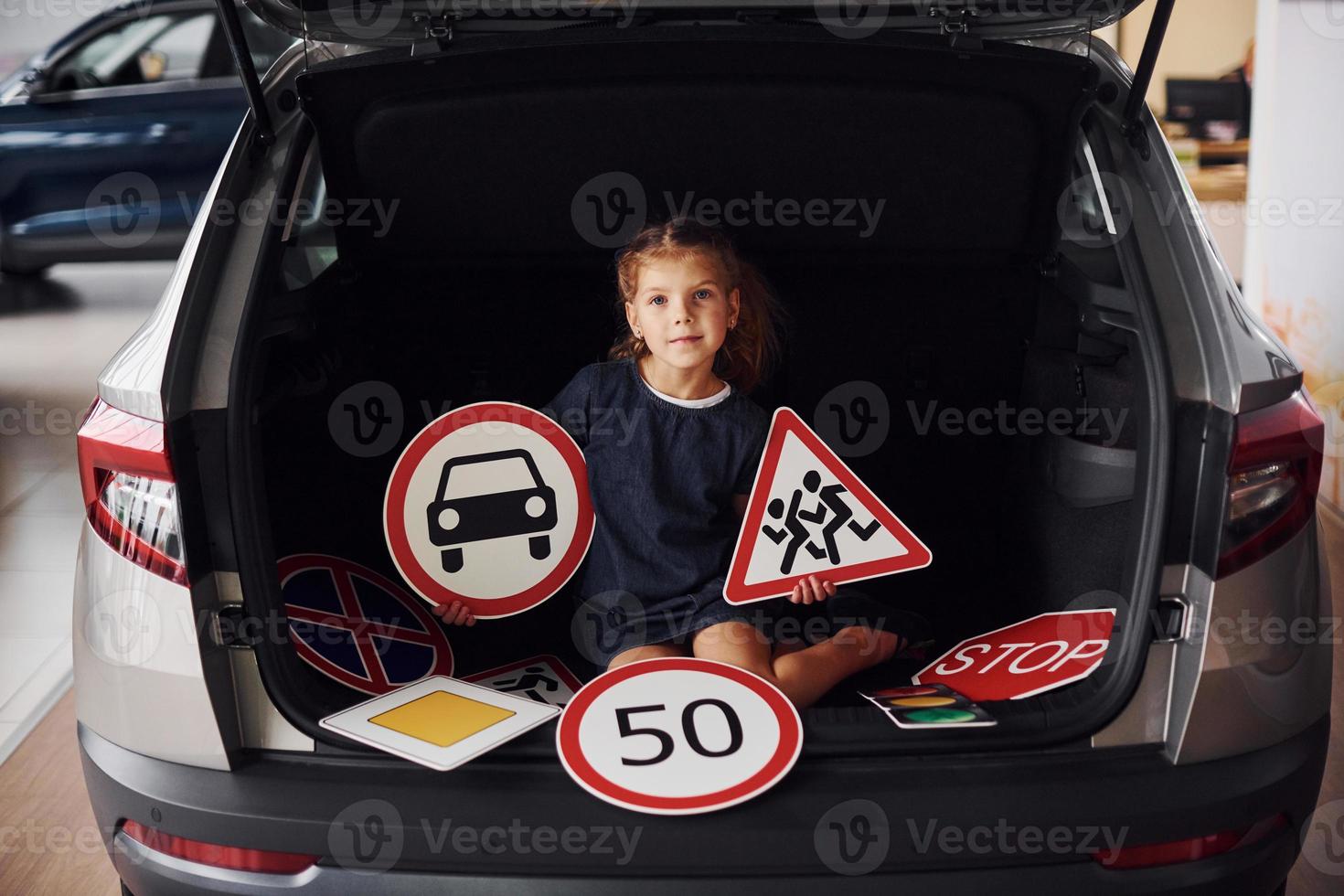 Portrait of cute little girl that holds road signs in hands in automobile salon photo