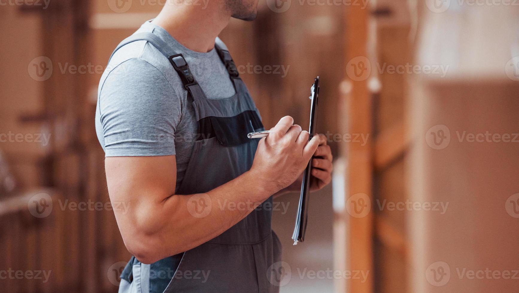 Storage worker in uniform and notepad in hands checks production photo