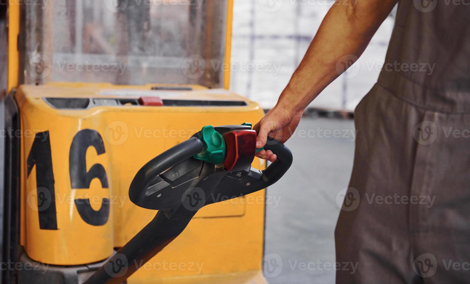 Young male worker in uniform is in the warehouse pushing pallet truck photo