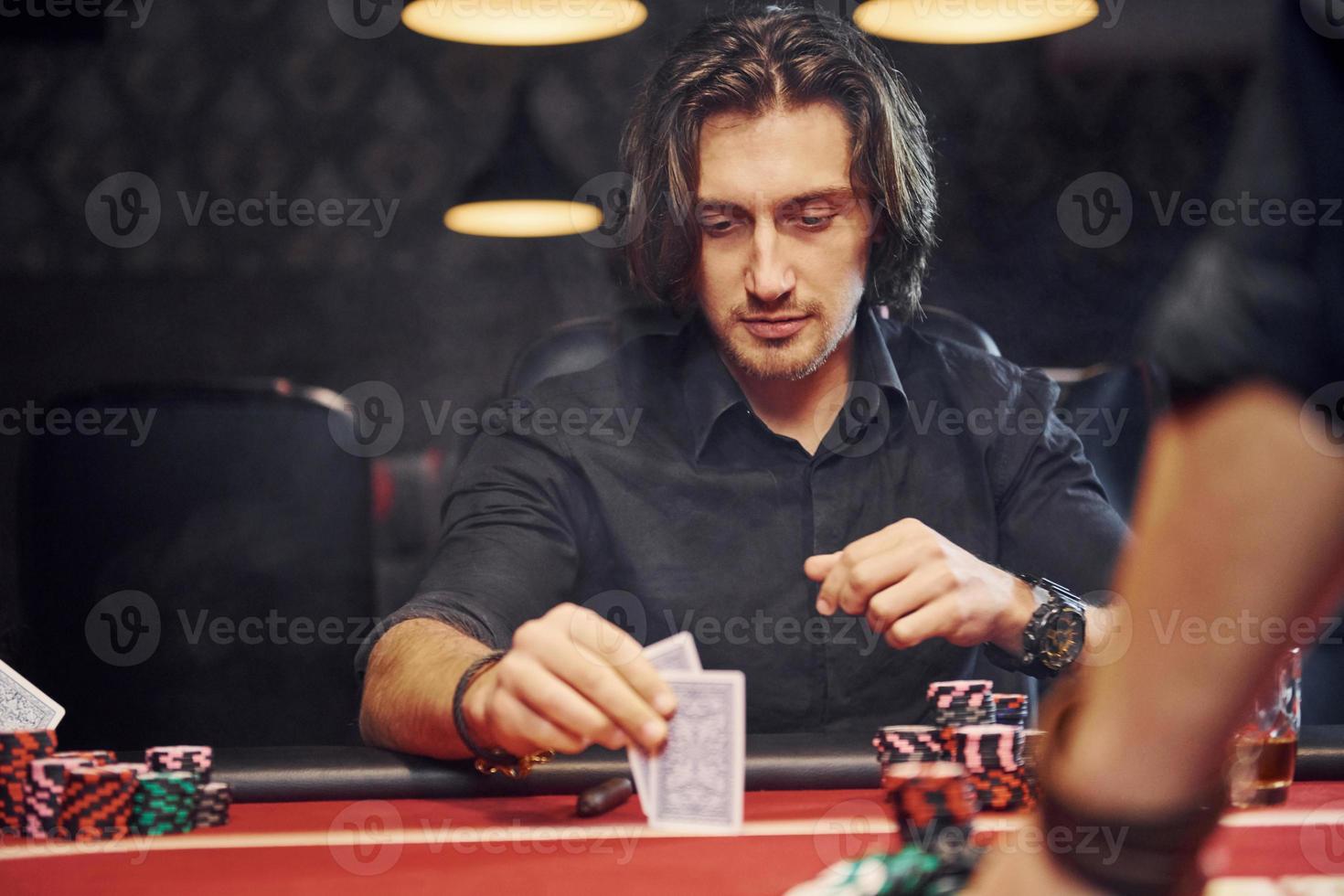 Elegant young people sits by table and playing poker in casino with smoke in the air photo