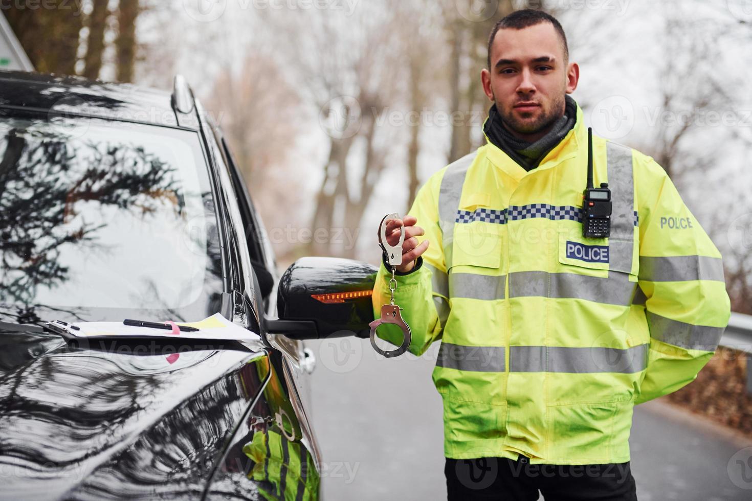 Male police officer in green uniformstanding with handcuffs near automobile photo