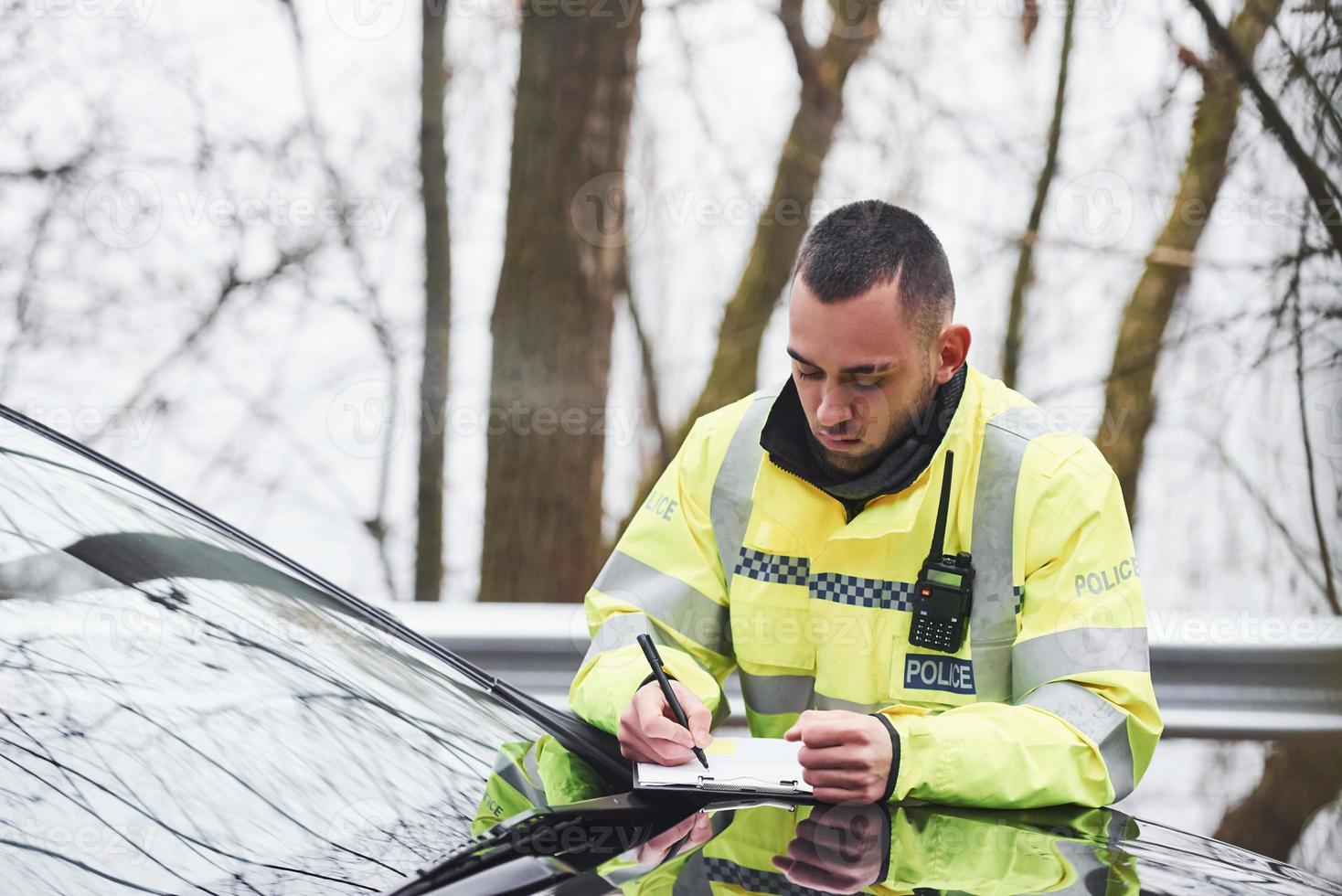 Male police officer in green uniform checking vehicle on the road photo