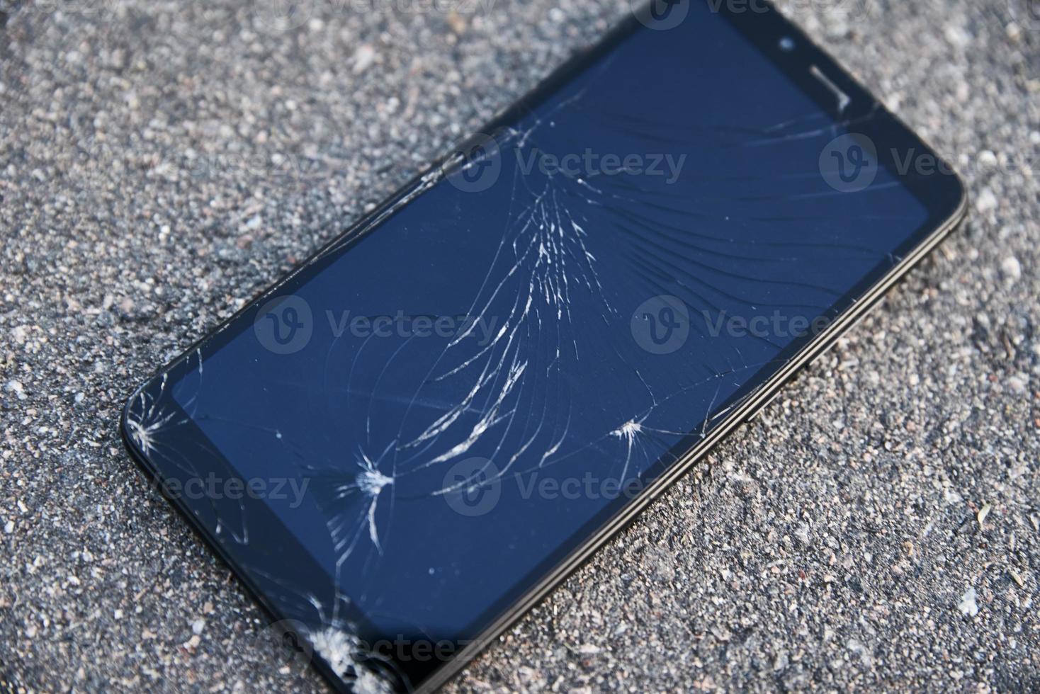 Damaged smartphone with broken touch screen on asphalt photo
