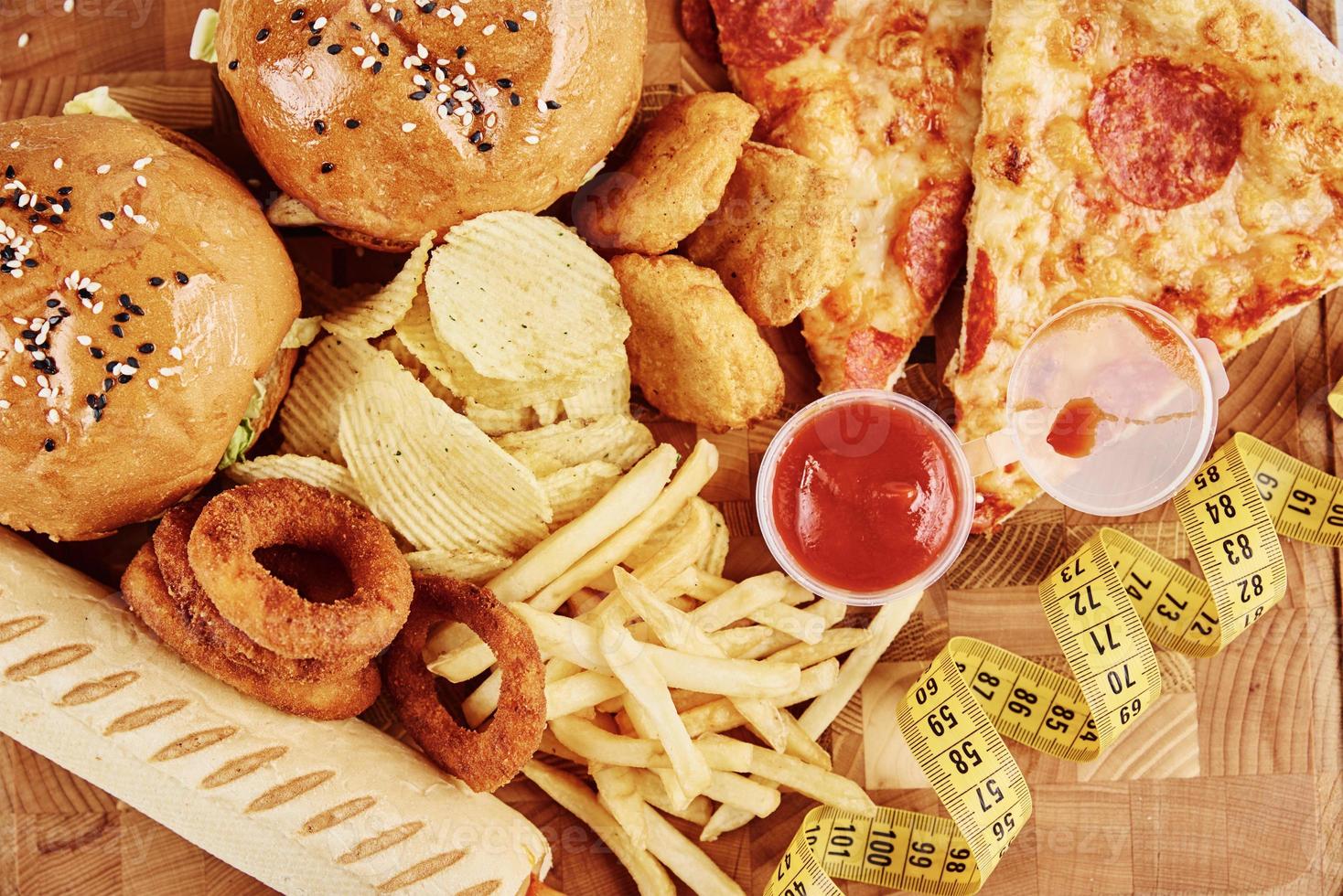 Different types of fastfood and snacks on the table with measuring tape photo