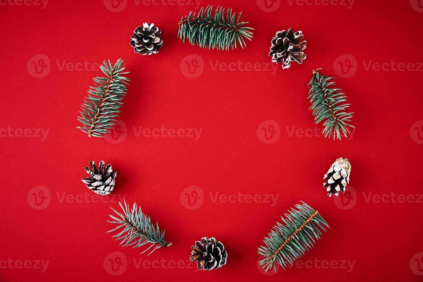 Wreath made of fir tree branches and festive pine cones on red background photo