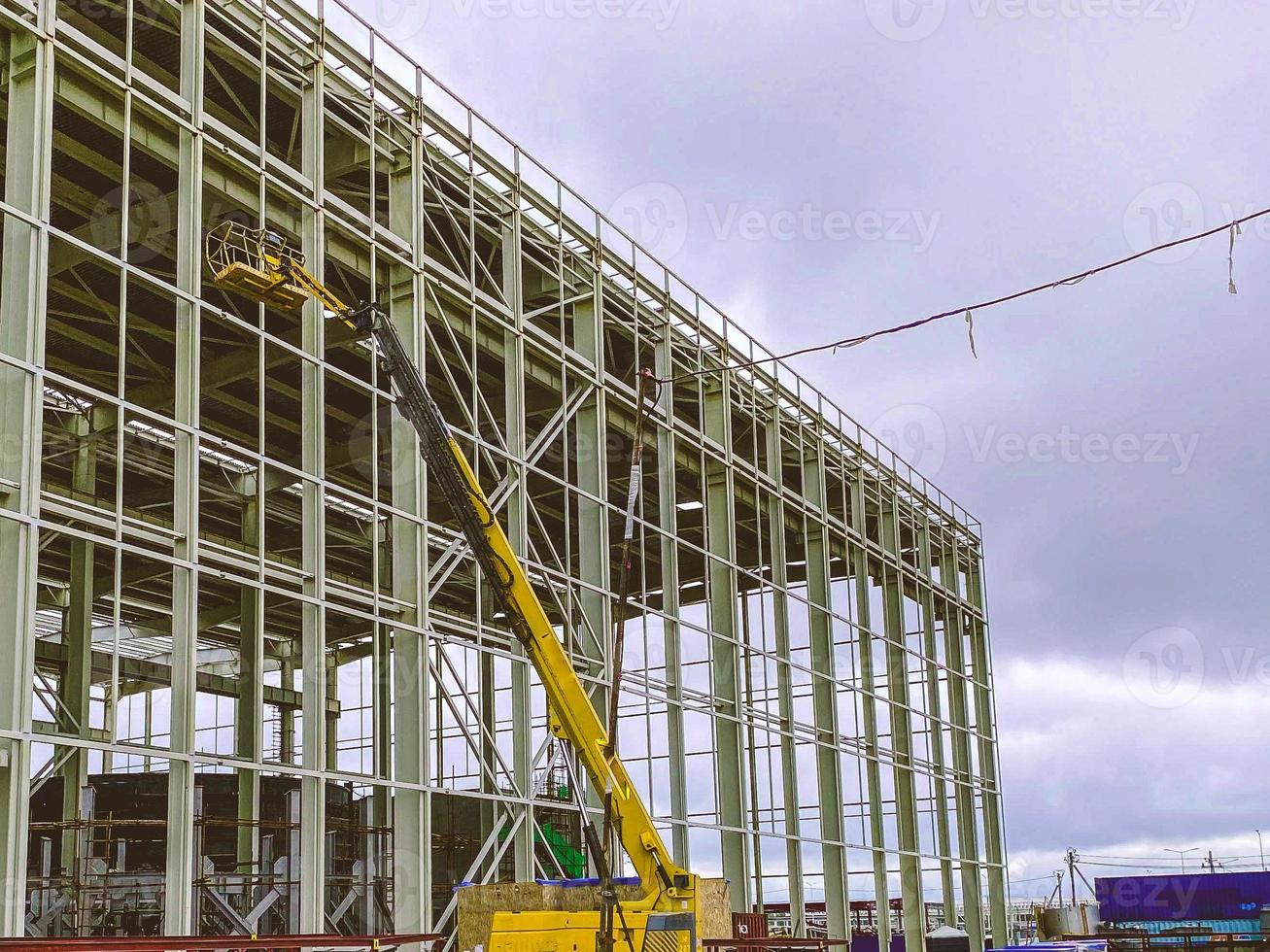 construcción de un nuevo complejo en la planta. Estructuras metálicas para la construcción de un nuevo edificio. grúa amarilla transporta material pesado por el aire foto