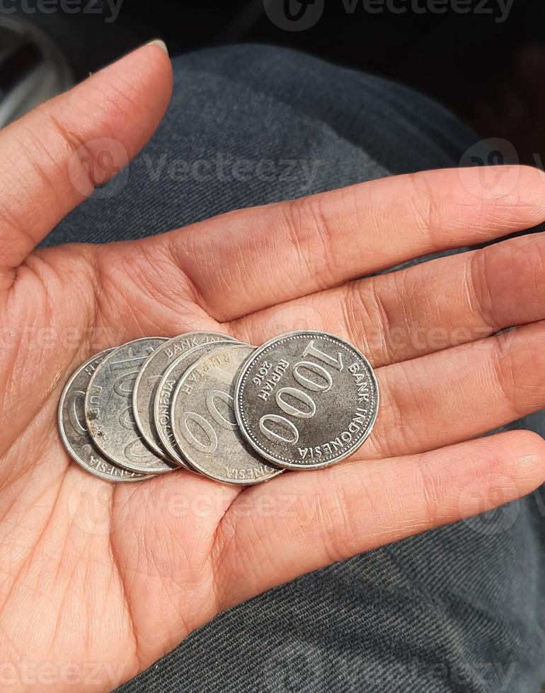 A hand is holding several rupiah coins. These coins are usually used to give to packs of people who help cross the vehicle or direct them to turn around. photo