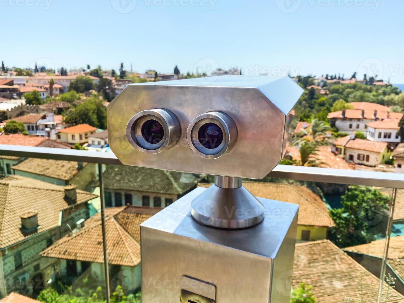 at the height of the houses of local residents with a tile roof. binoculars for tourists are installed on the roof. binoculars on a metal pedestal with black lenses photo