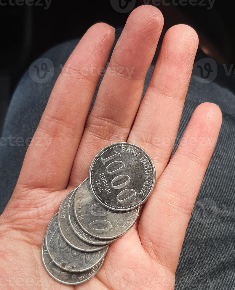 A hand is holding several rupiah coins. These coins are usually used to give to packs of people who help cross the vehicle or direct them to turn around. photo