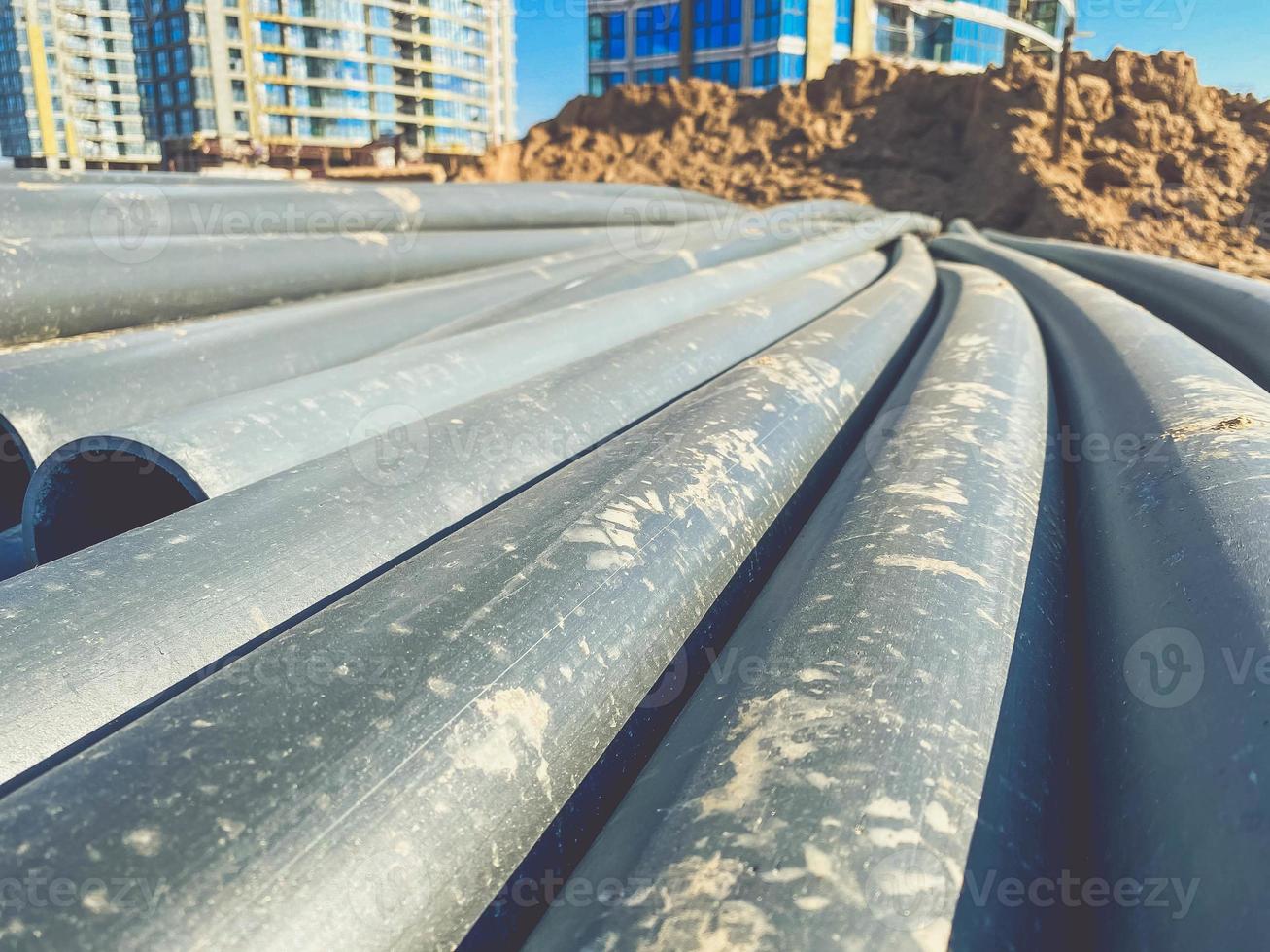 pipes for the construction of communications in the new microdistrict. black plastic pipes in sand and debris. long pipes for water and waste disposal photo