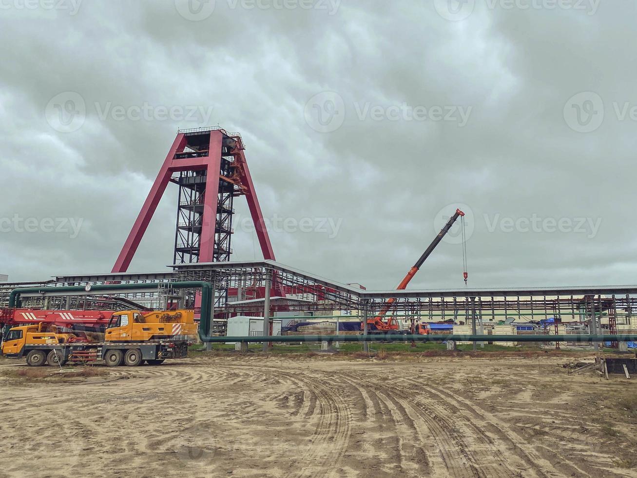 complejo minero. taladro de metal para buscar minerales en el suelo. construcción en el polígono industrial de la planta. grúas y equipos de construcción cercanos, la construcción del complejo foto