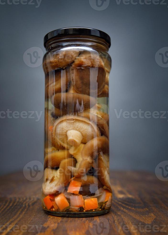 Pickled mushrooms with vegetables in a glass jar . Salted homemade mushrooms . Rustic food . photo