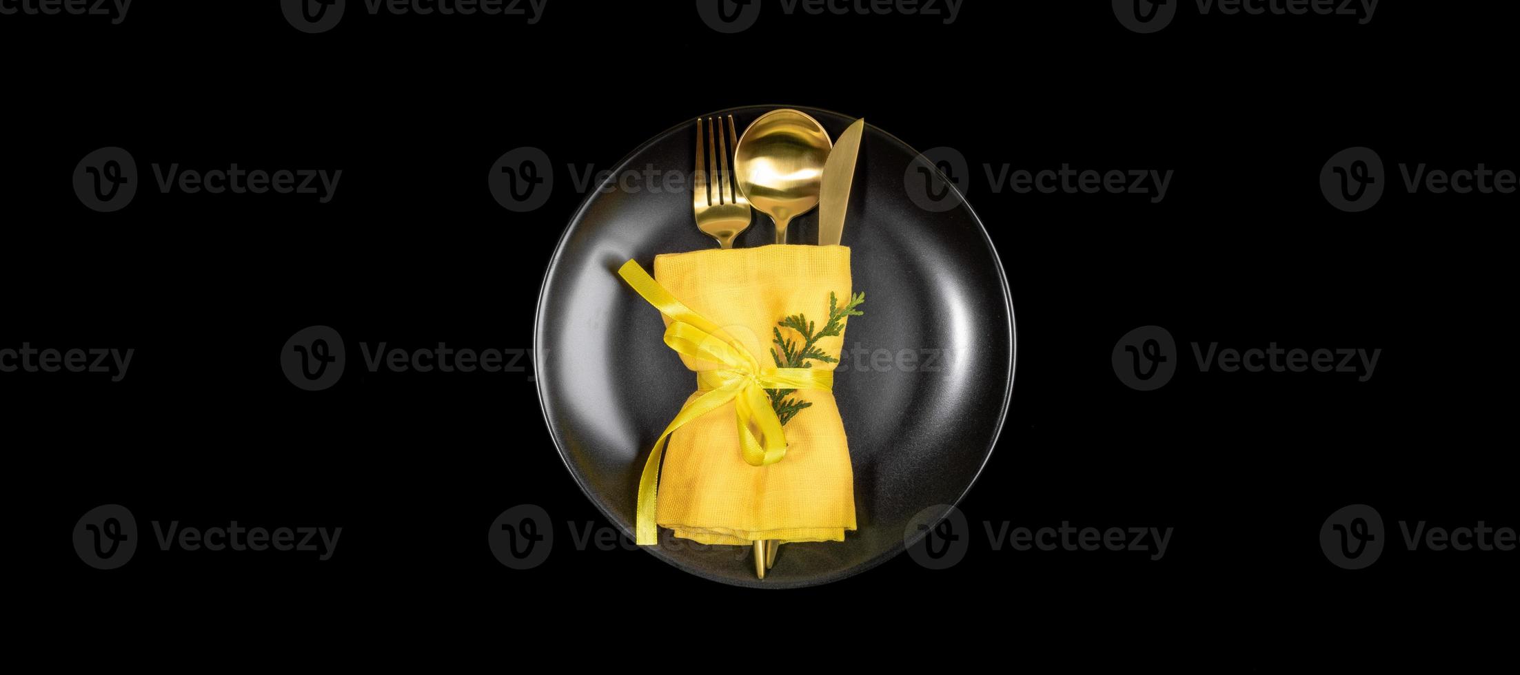 Xmas table setting banner with golden cutlery set on round black plate in center of black. photo