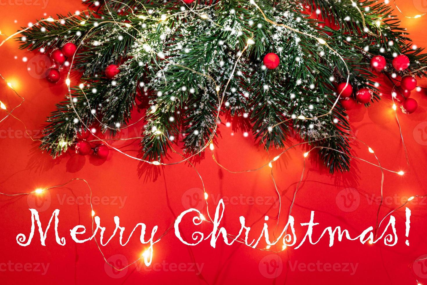 tarjeta de felicitación festiva de navidad con ramas de abeto, nieve, bayas rojas, luces de navidad en rojo con el título feliz navidad. foto
