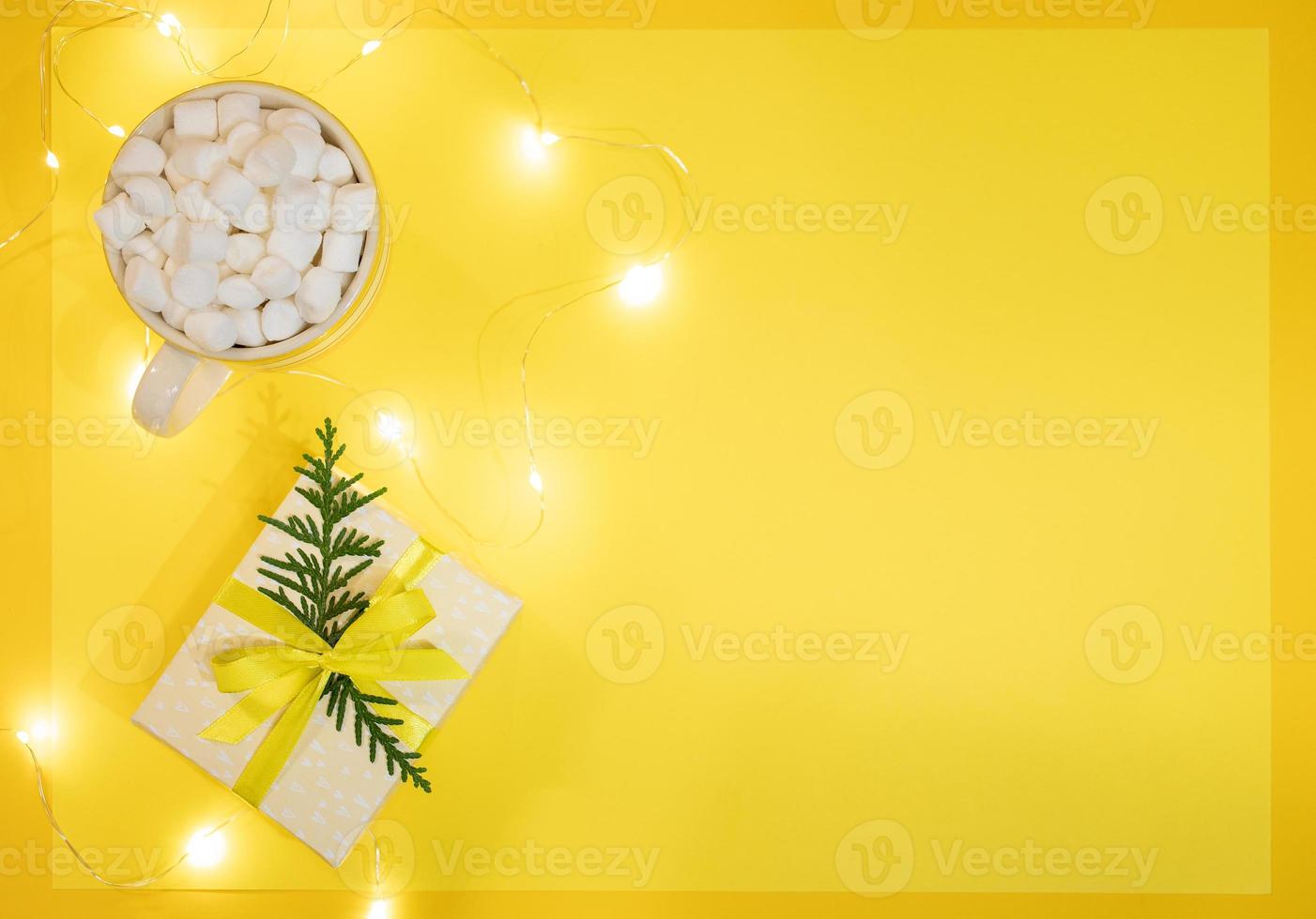 Xmas festive yellow background with cup of coffee or cocoa with marshmallows, DIY gift box and luminous Xmas lights. photo