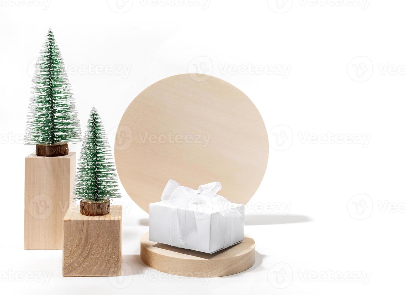 Trendy minimal Xmas composition with decorative Xmas tree and DIY gift box on wooden podiums on white with copy space. photo