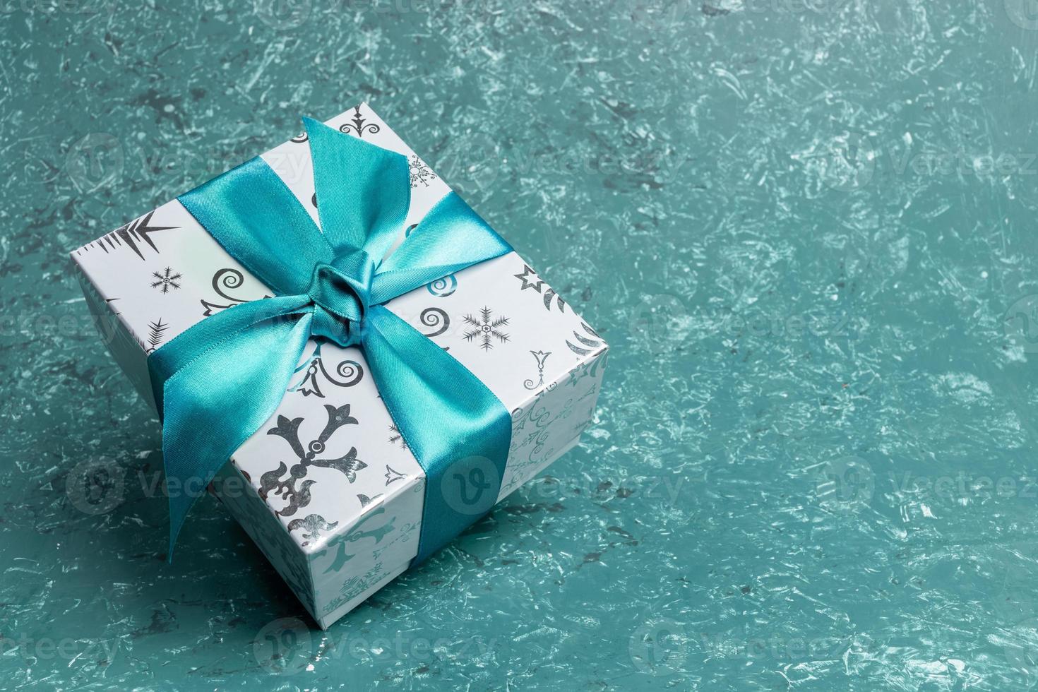 Patterned gift box with DIY bow on turquoise textured background. Christmas or New Year monochrome image. photo