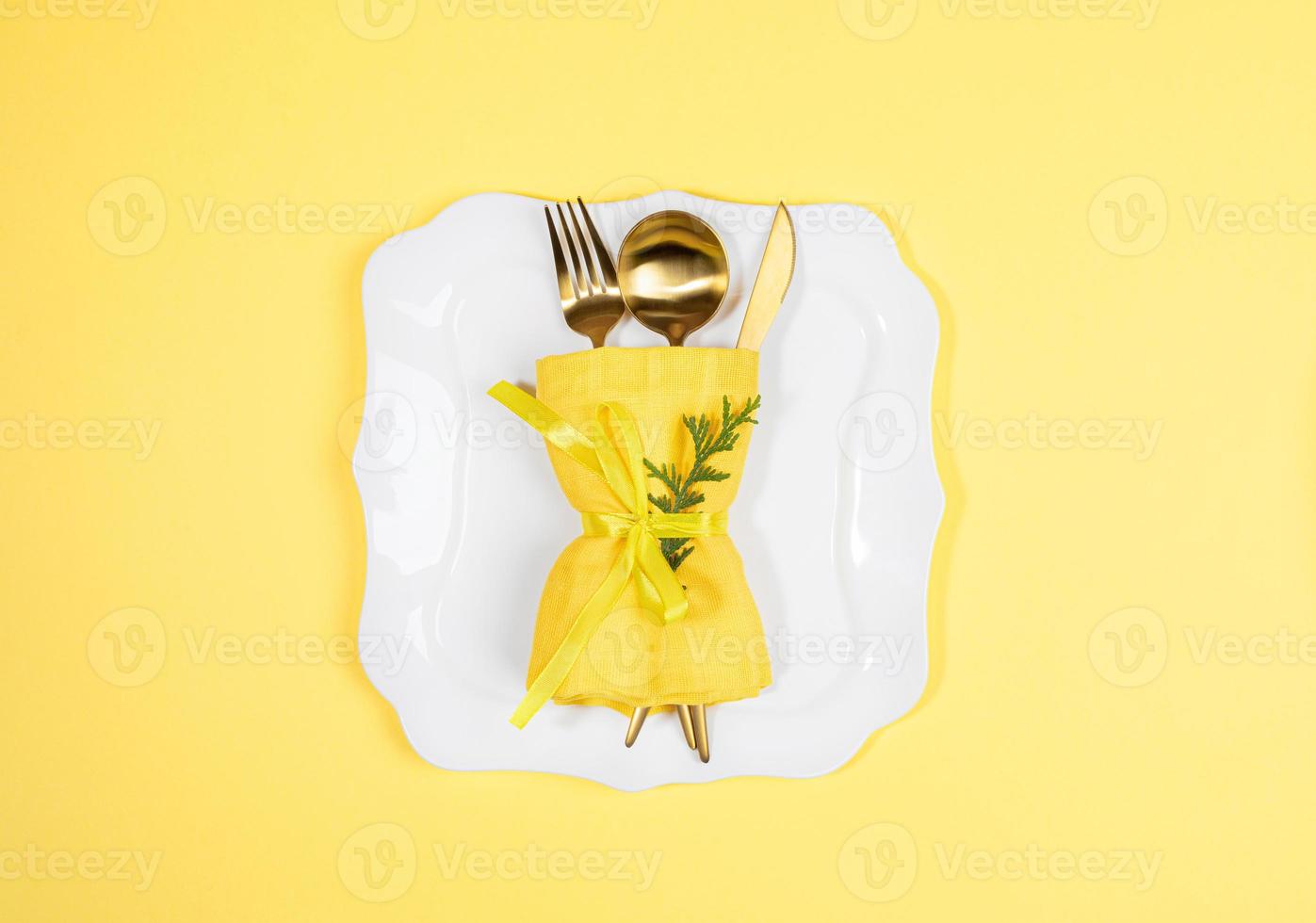 Christmas table setting with gold cutlery set on white figured plate on yellow. Copy space. photo