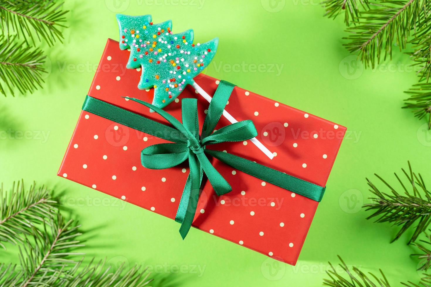 Red in polka dots wrapped box decorated with green ribbon, bow and lollipop as Xmas tree on green. photo