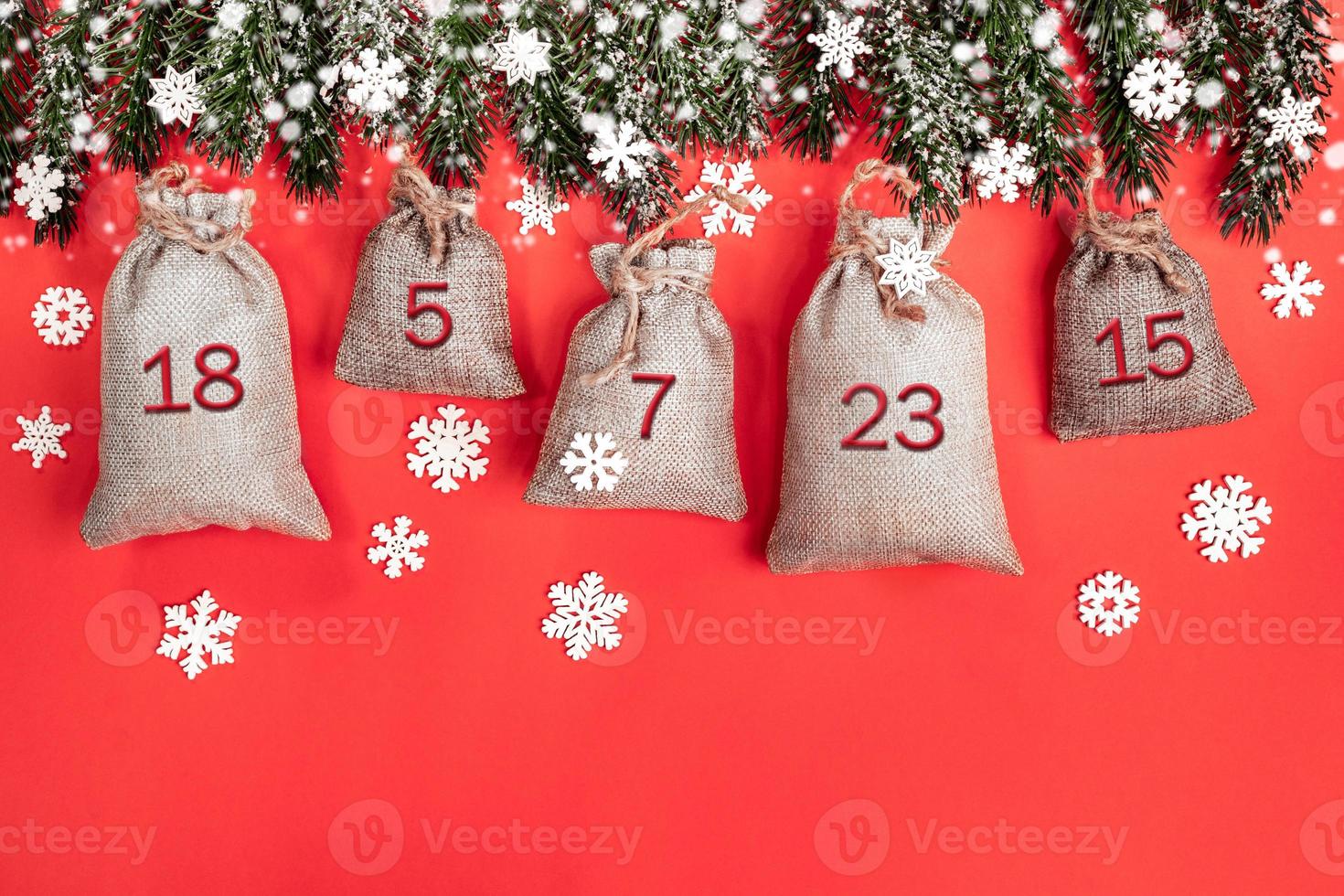 Xmas advent calendar - canvas sacks with numbers on fir tree branches, snowflakes and snow on red. photo