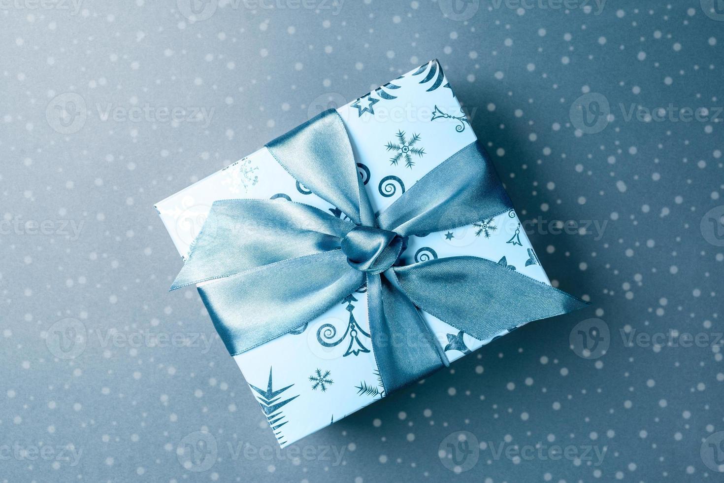 Patterned gift box with DIY bow on turquoise backdrop with drawn snow. Holiday festive monochrome image. Christmas or New Year background. Horizontal orientation. Top view. photo