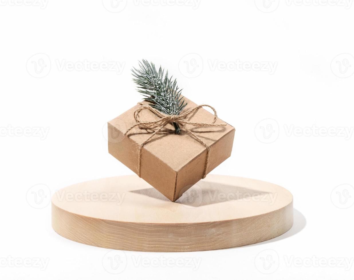 Xmas holiday composition with one DIY gift cardbox balanced on round wooden stand on white background. photo
