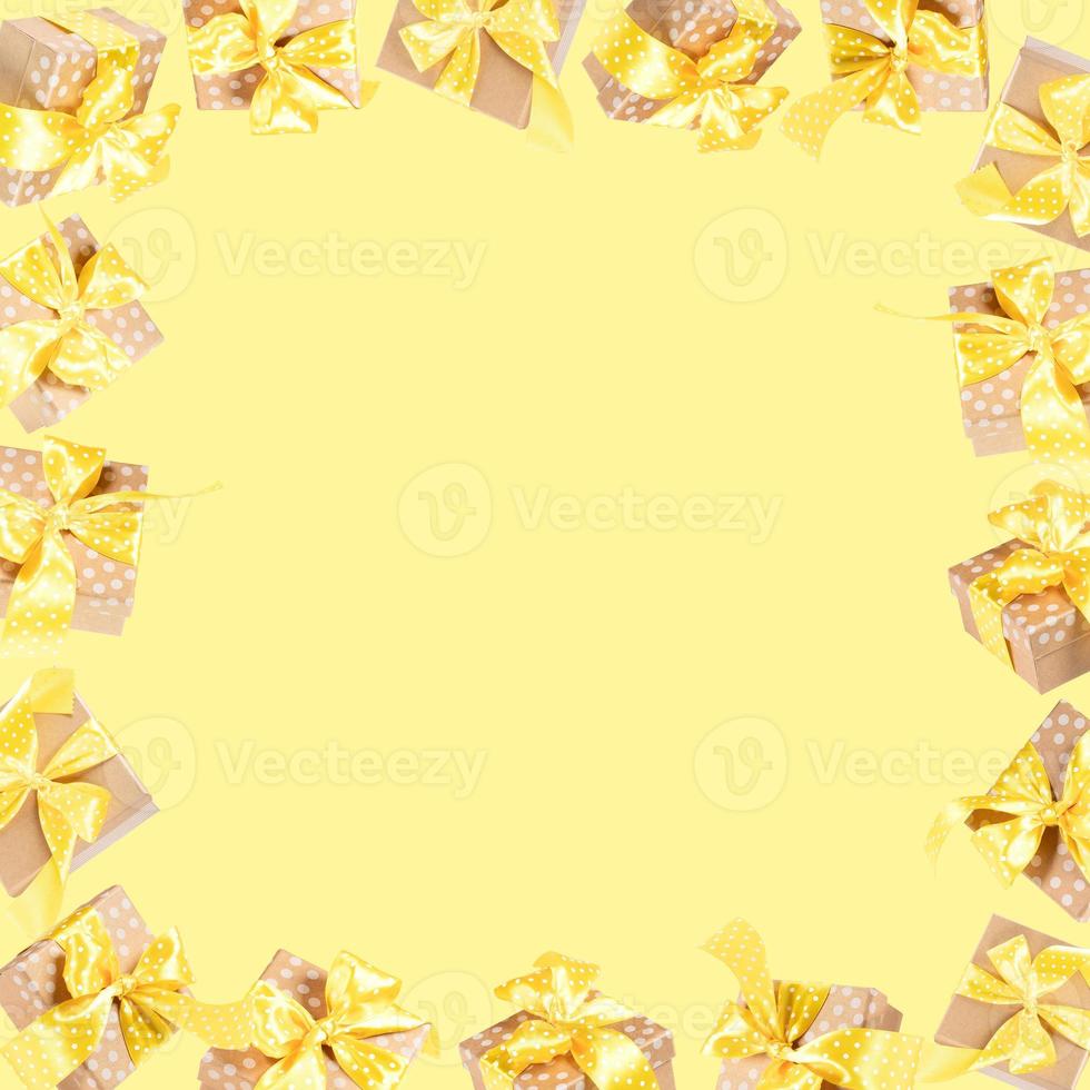 Frame of wrapped gift boxes from craft papers with yellow polka dot bows on yellow with copy space. photo