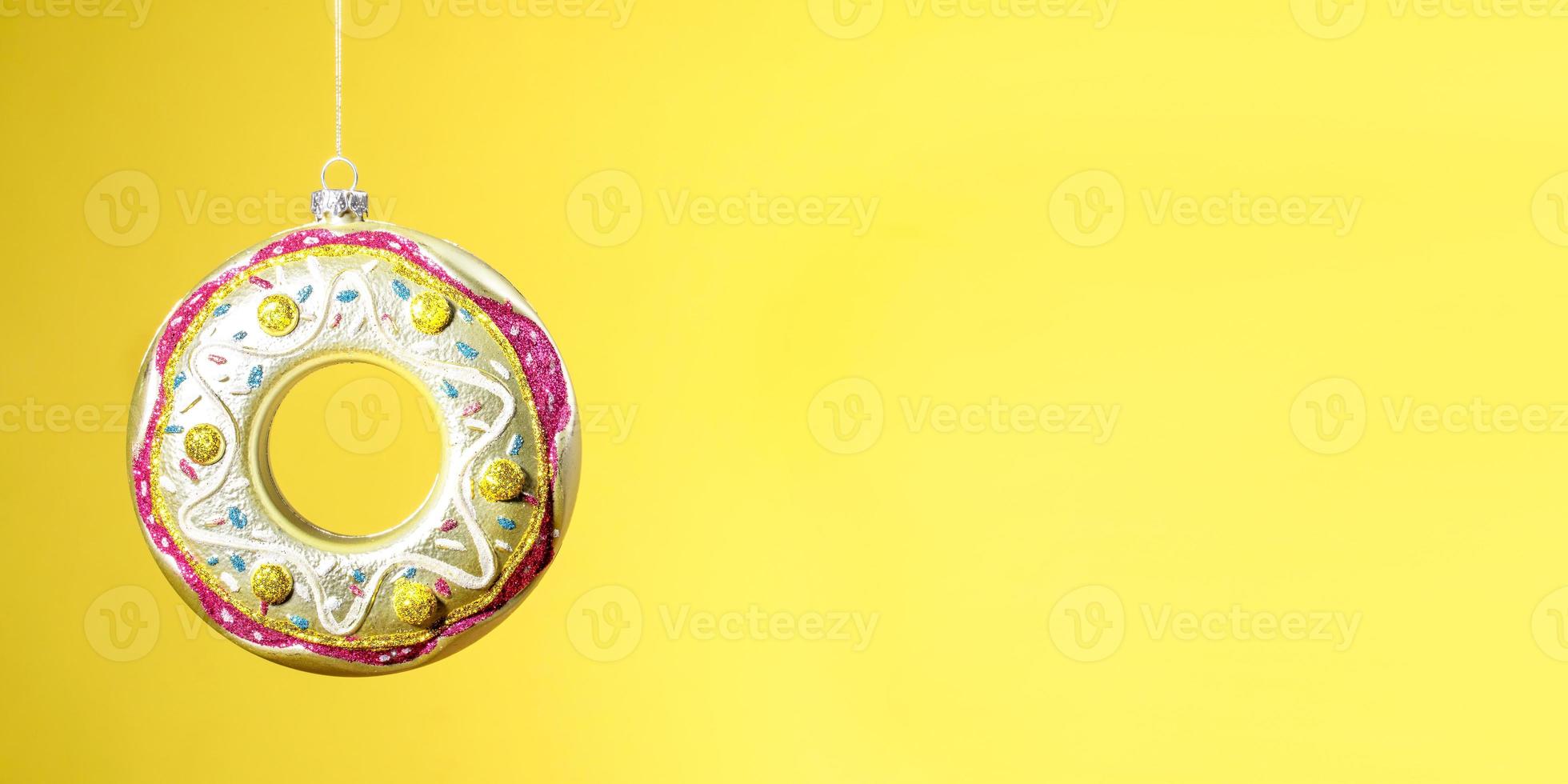 Christmas creative minimal banner with one hanging glass Xmas toy donut on yellow with copy space. photo