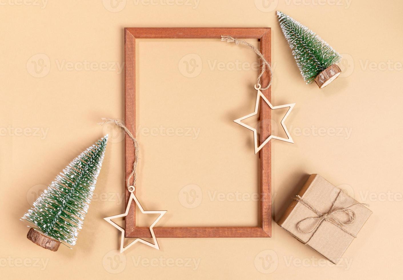 Christmas or New Year festive arrangement of empty wooden frame, wooden festive decorations and gift box on beige. photo