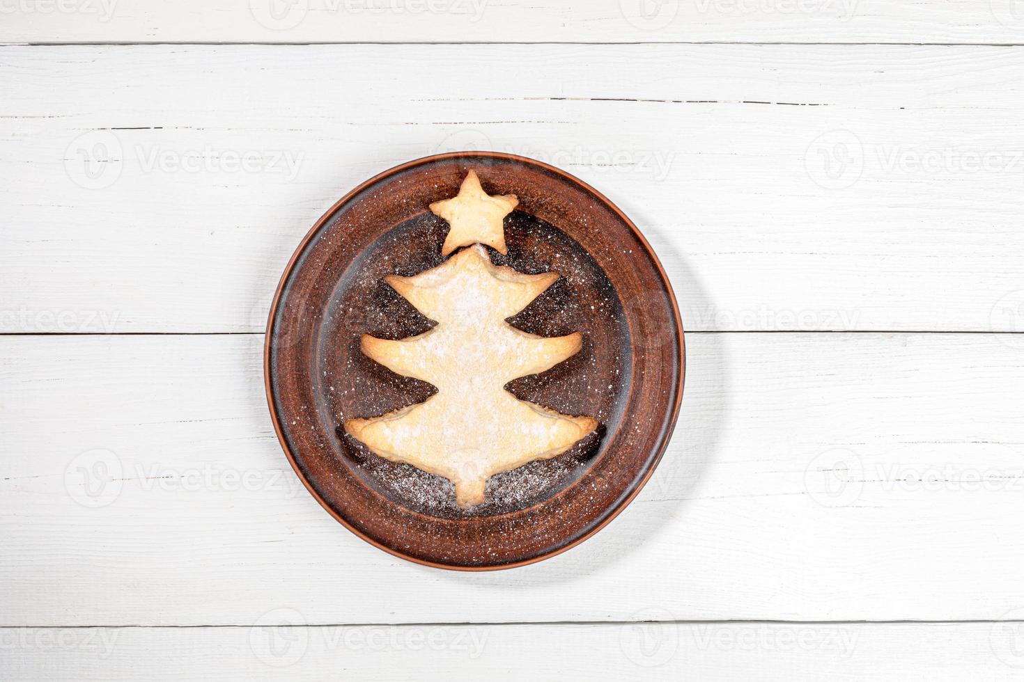 Homemade cookie as Christmas tree on round brown plate on white wooden backdrop with copy space. photo