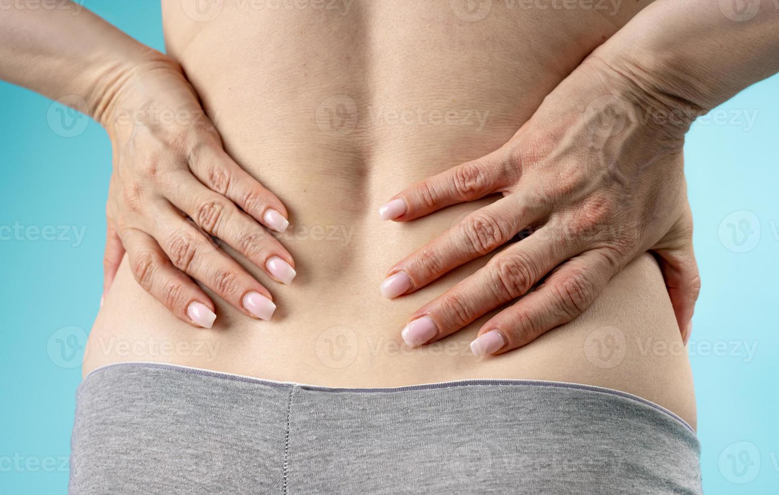 woman holding hands on her lower back feeling big pain. isolated on  purple  background photo