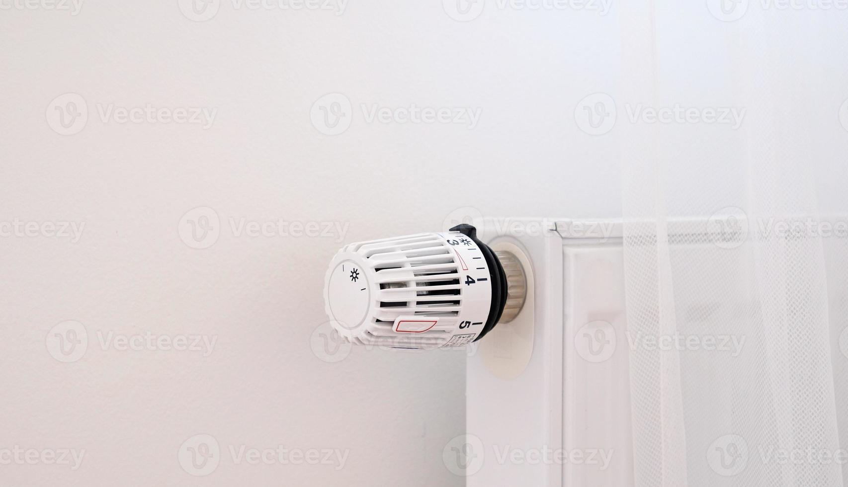 Banner with thermostat and battery temperature controller. Heating service cost concept, utility price increase. Temperature control valve. White heater on wall with curtain in modern apartment. photo