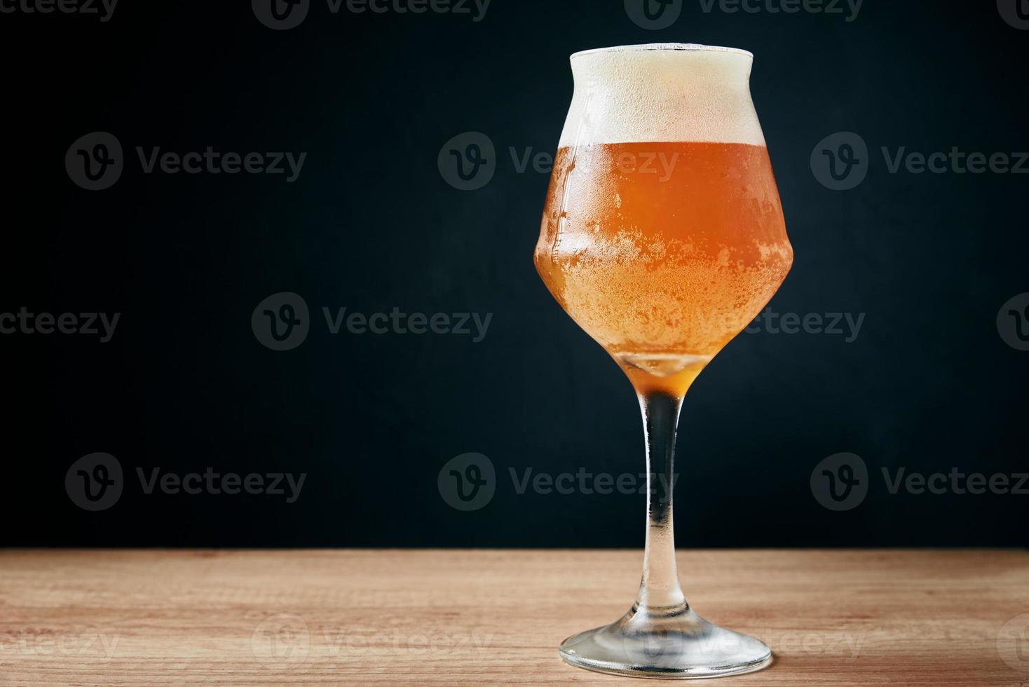 Glass of cold beer with foam on dark background photo