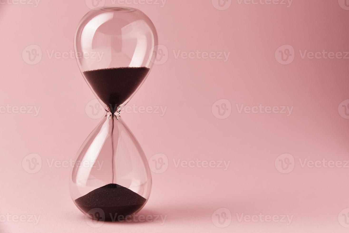 Hourglass on pink background, closeup. Urgency and running out of time concept photo