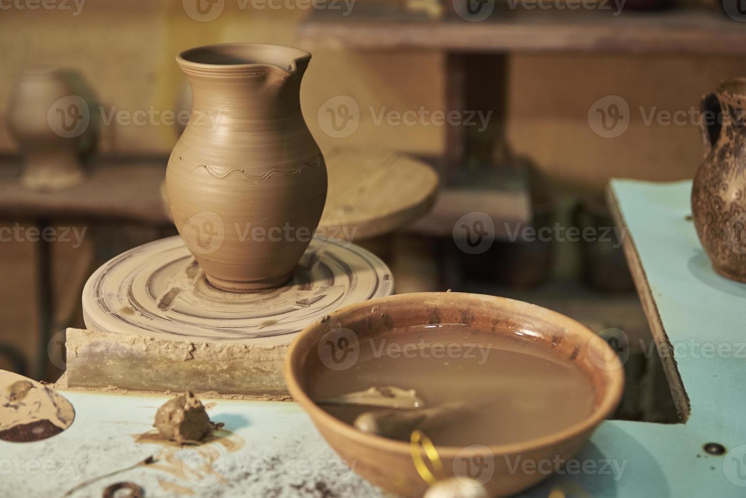 Clay pot on potter's wheel in workshop interior photo