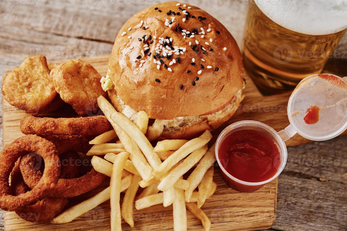 Different types of fastfood and snacks and glass of beer on the table photo