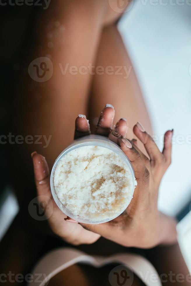 Black-skinned model dressed in underwear holds a jar with a scrub photo