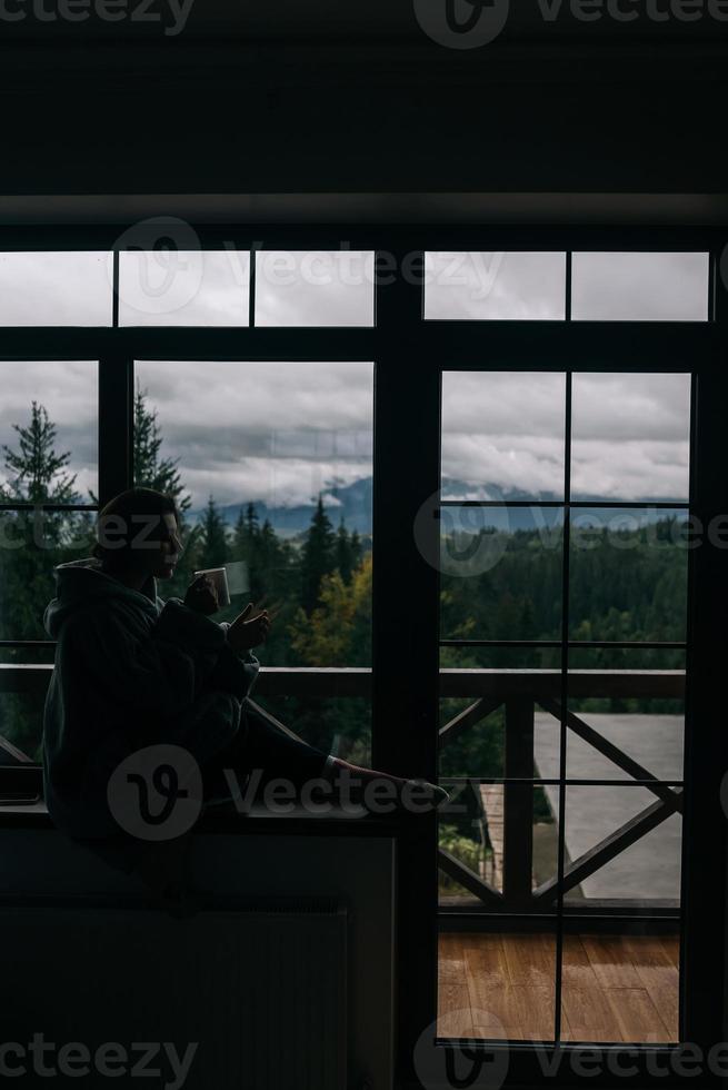 Silhouette of a woman sitting on the windowsill with a mug photo