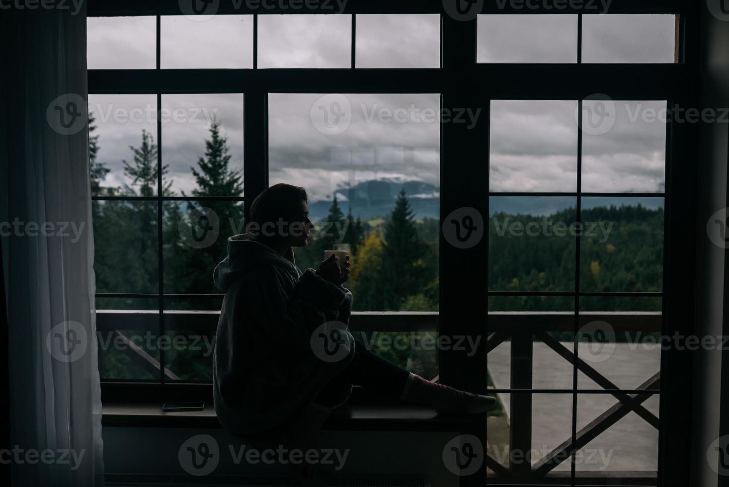 Silhouette of a woman sitting on the windowsill with a mug photo