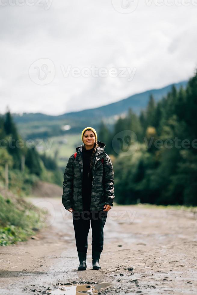 modelo de hipster femenino saludable activo senderismo a lo largo de la carretera de montaña del bosque. foto