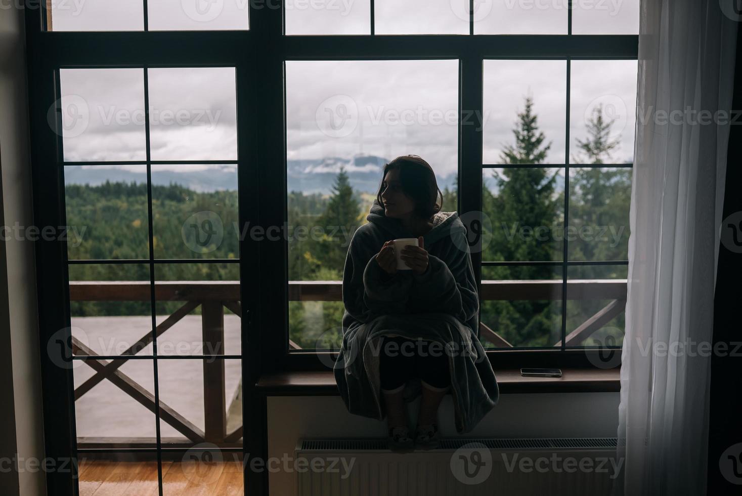 silueta de una mujer sentada en el alféizar de la ventana con una taza foto