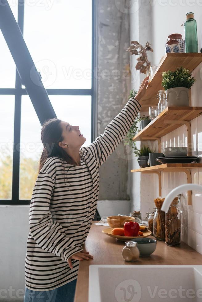 Woman takes out a glass from shelf in the kitchen photo