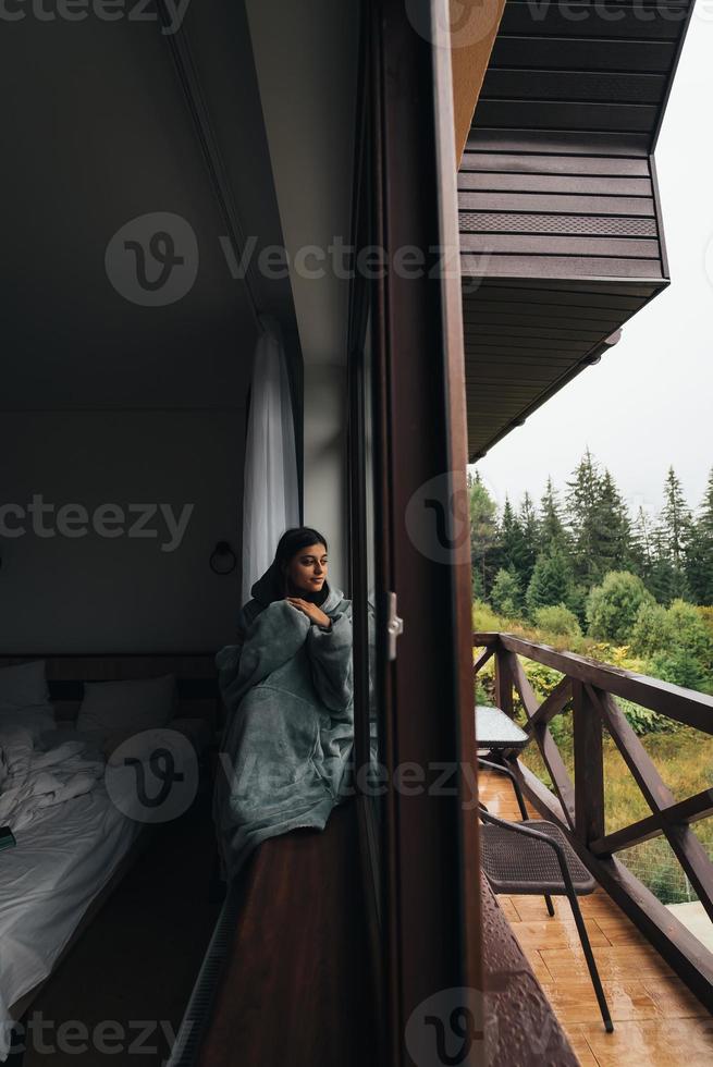 Woman sits on the windowsill and looks at the mountains photo