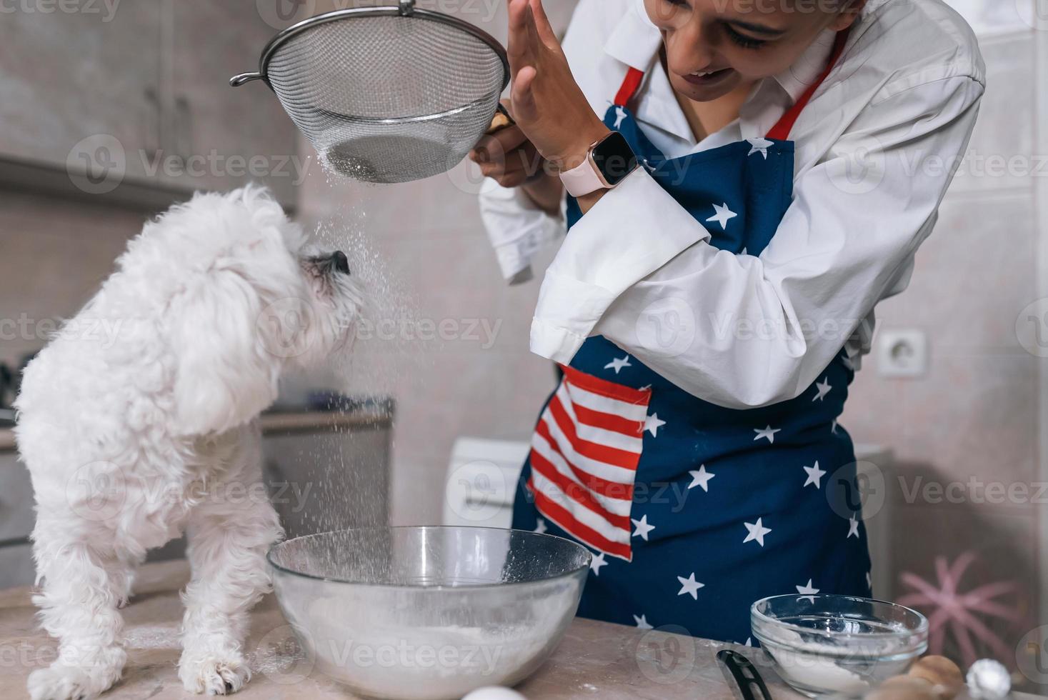 mujer en la cocina tamiza la harina junto con un perro foto